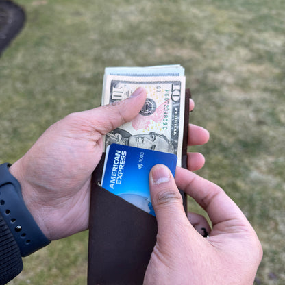 Person holding a wallet with money and an American Express card against a grassy background
