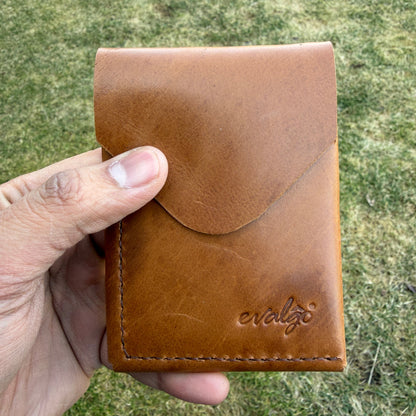 Brown leather wallet held in a hand with a grassy background