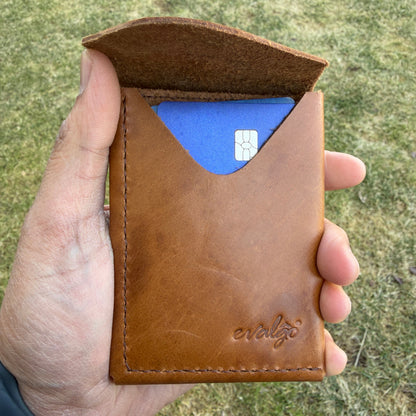 Brown leather cardholder with a blue card inside, held in a hand against a grassy background.
