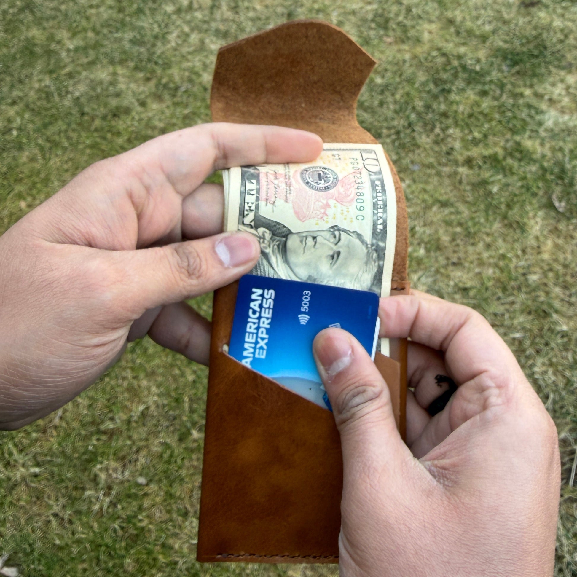 Person holding a wallet with money and a card against a grassy background