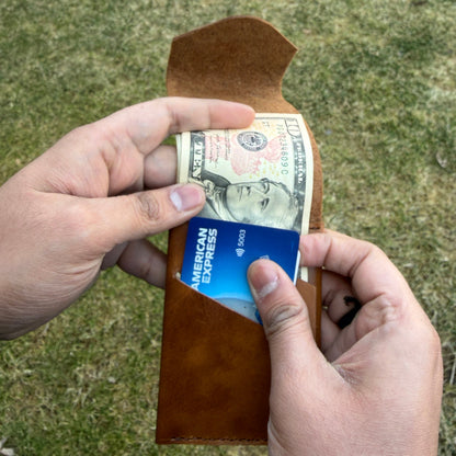 Person holding a wallet with money and a card against a grassy background