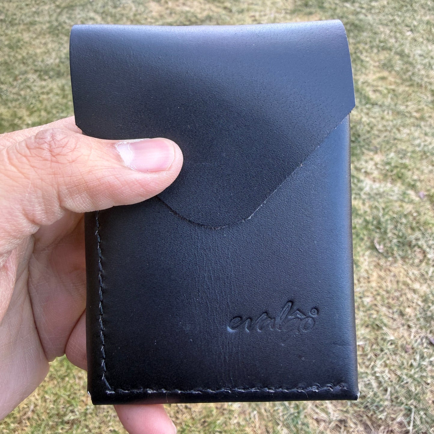 Black leather wallet held by a hand with grassy background